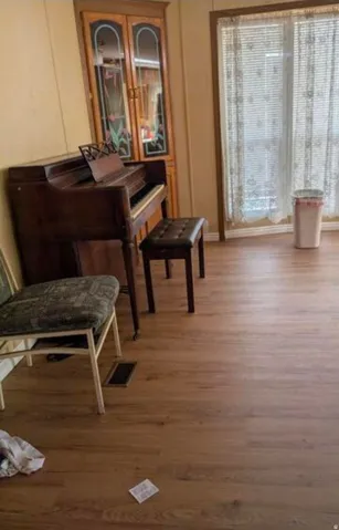 Wood-finish flooring throughout, complemented by a built-in corner cabinet with glass-paneled doors, and a large window providing natural illumination