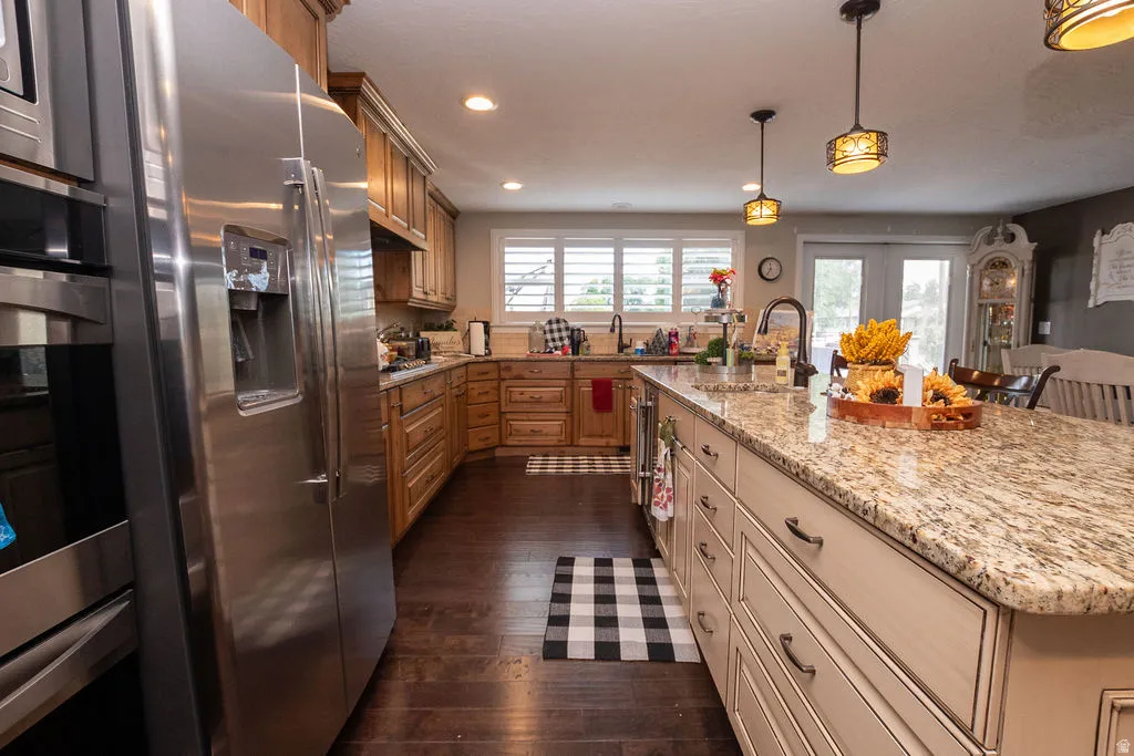 Kitchen featuring dark wood-finish flooring, stainless steel appliances, wood cabinetry, a center island with a light-toned countertop, and recessed lighting
