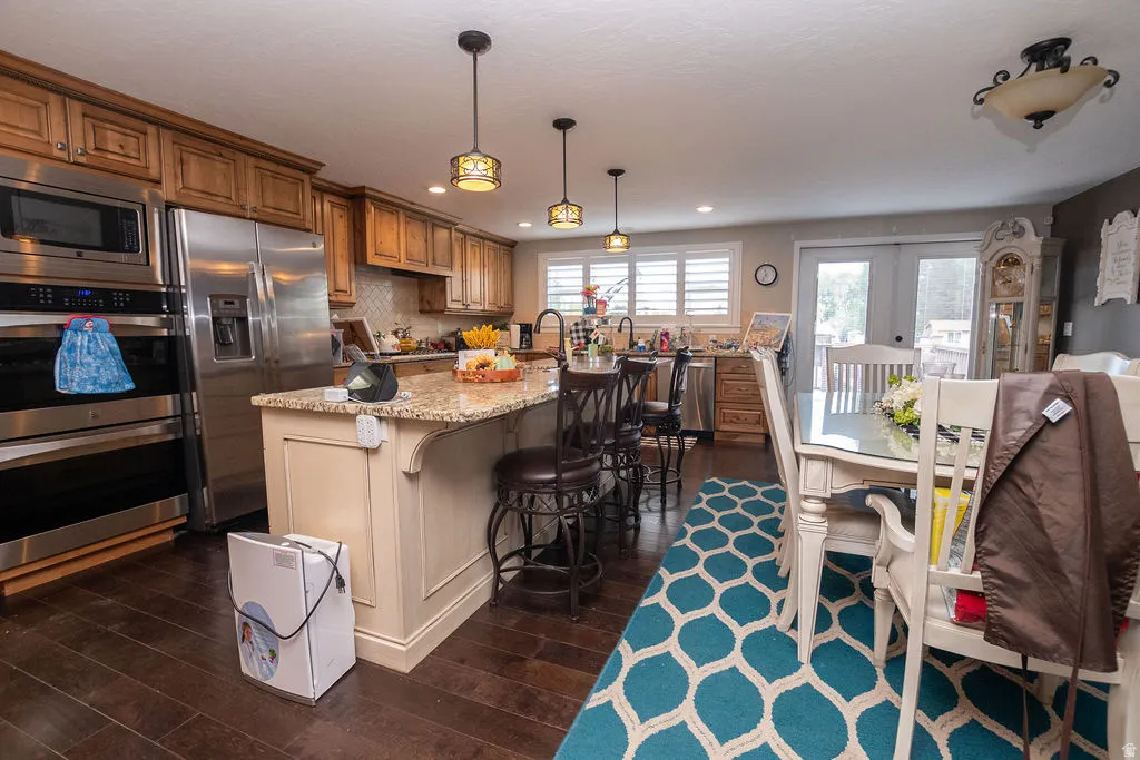 Kitchen featuring wood-finish flooring, stainless steel appliances, a kitchen island with seating, pendant lighting, and light-toned cabinetry