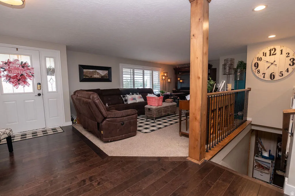 Wood-finish flooring, white entry door with decorative glass, and a wood pillar