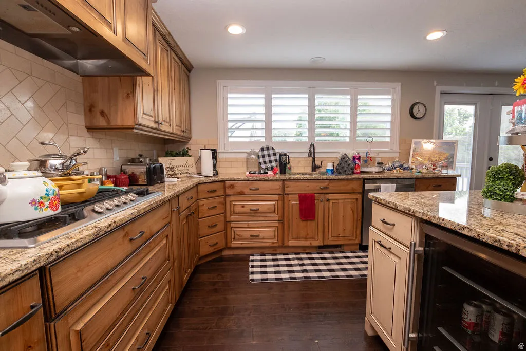 Kitchen featuring wood cabinetry, granite countertops, tile backsplash, built-in range, and a beverage cooler