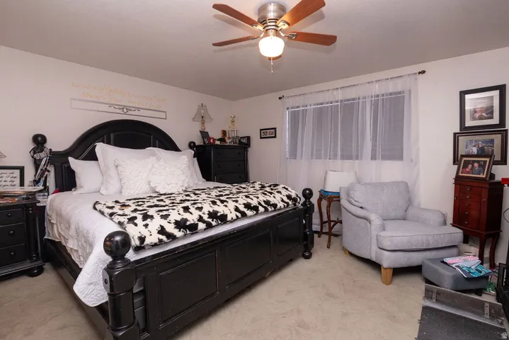Ceiling fan with wooden blades, window with sheer white curtains, and light-colored carpeting