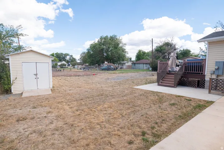 Detached storage shed with double doors, wood-finish raised deck, concrete patio, and concrete pathway
