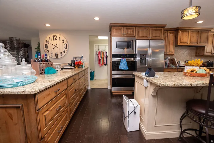 Kitchen featuring wood-finish flooring, granite countertops, wood cabinetry, and stainless steel appliances including a built-in microwave and double ovens
