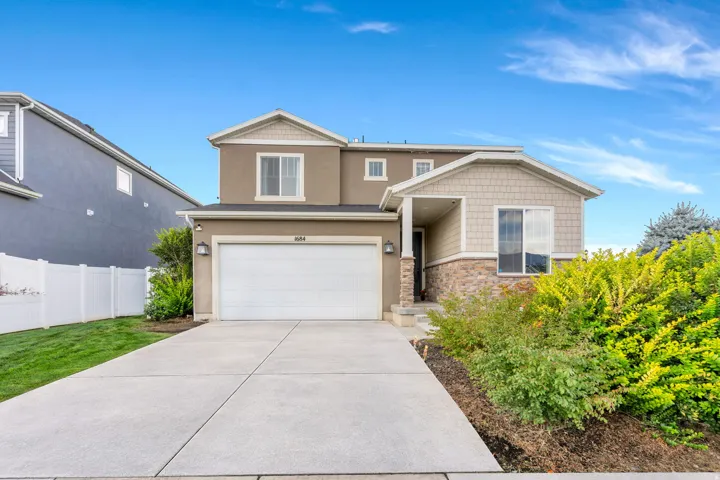 Two-story stucco and shingle exterior with stone accents, featuring a two-car garage, concrete driveway, and front landscaping