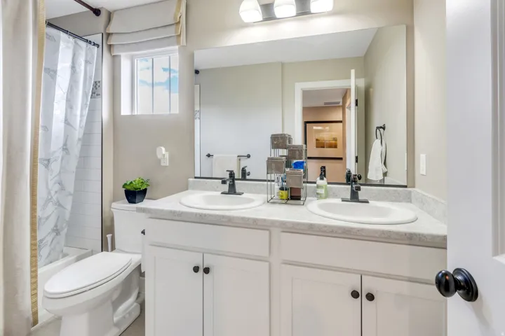 Dual vanity with white cabinetry and dark hardware, integrated sinks, and a full-width mirror
