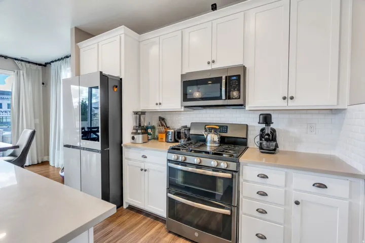 White shaker-style cabinetry with dark hardware, light countertops, wood-finish flooring, and a subway tile backsplash
