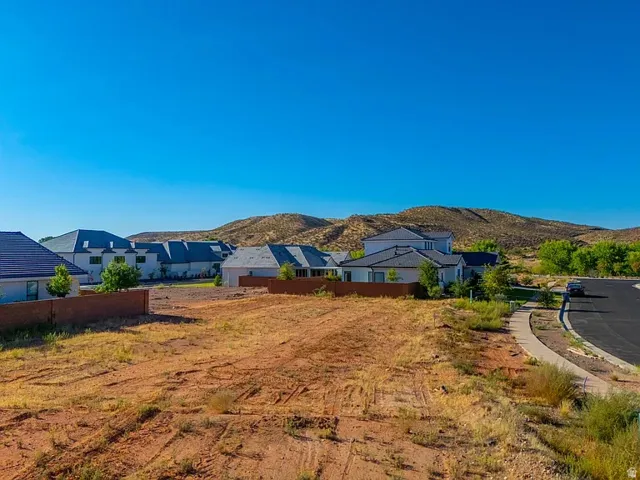 Cleared building lot with surrounding residential properties, paved street, and sidewalk