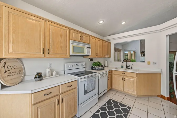 Wood-finish cabinetry with dark hardware, white countertops, built-in microwave, white electric range, and tile flooring