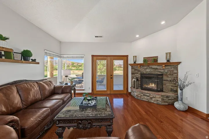 Hardwood flooring, corner stone fireplace with wood mantel, recessed lighting, and French doors leading to exterior