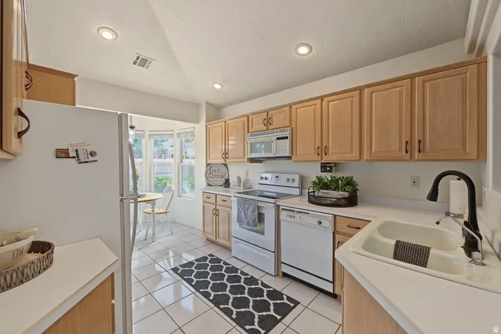Recessed lighting illuminates this kitchen featuring light wood cabinetry, white countertops, and tile flooring