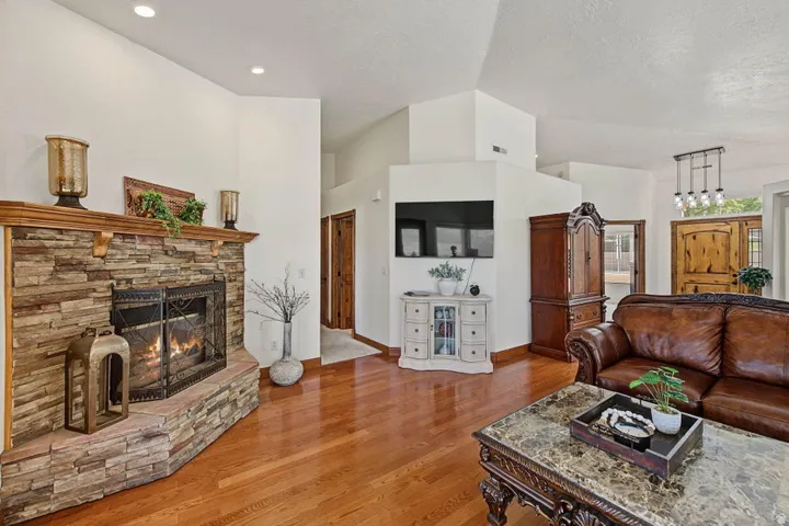 Stone-surround fireplace with a wood mantle, recessed ceiling lighting, wood-finish flooring, and a decorative front entry door