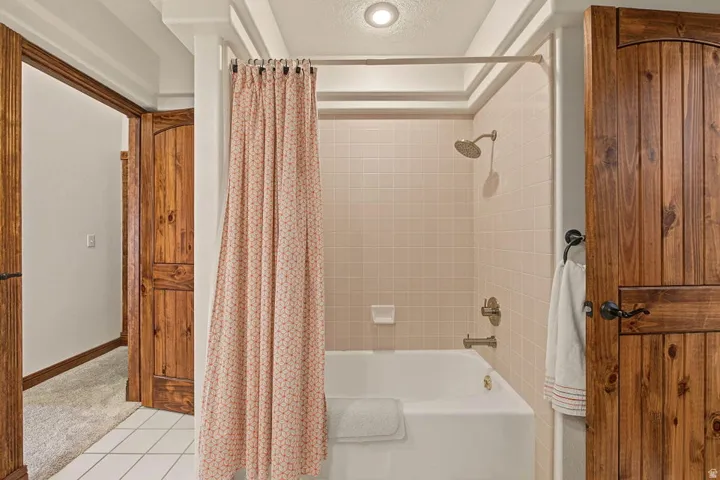 Tub and shower combination with tile surround, white tile flooring, and wood-paneled doors