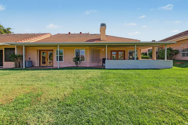 Expansive green lawn with a covered patio, multiple glass panel doors, and a partial low wall