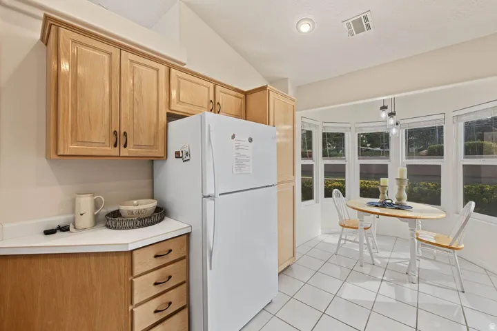 Wood-finish cabinetry, white countertops, tile flooring, vaulted ceiling, and a bay window