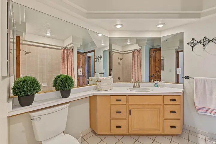 Recessed lighting, wood-finish cabinetry, integrated sink, tiled flooring, and a shower with tiled walls