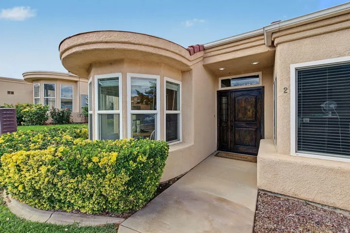 Stucco exterior with a curved bay window, dark wood double entry door, recessed lighting, and a concrete pathway