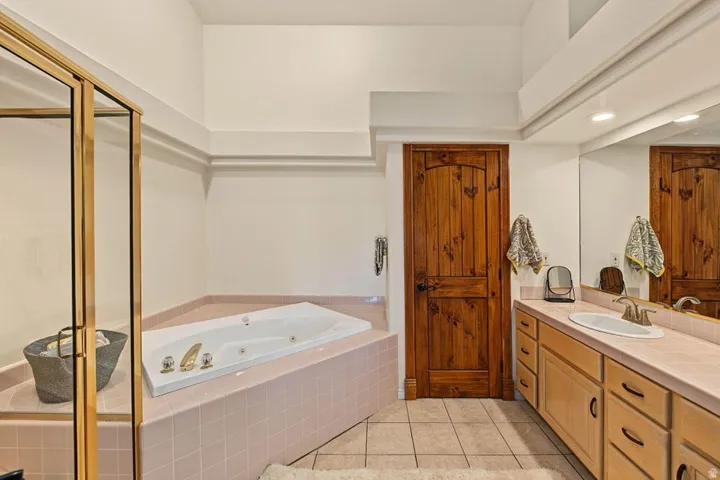 Built-in corner soaking tub with tiled surround, light wood-finish vanity with an integrated sink, brushed nickel faucet, and a full-width mirror