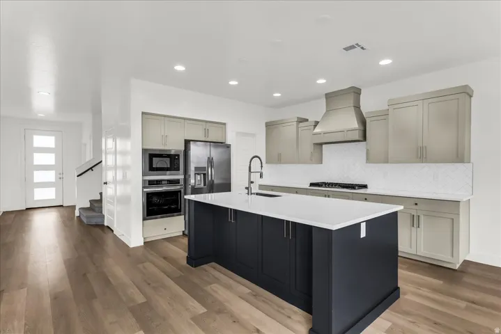 Contemporary kitchen featuring a center island with countertop, stainless steel appliances, a range hood, and a tile backsplash