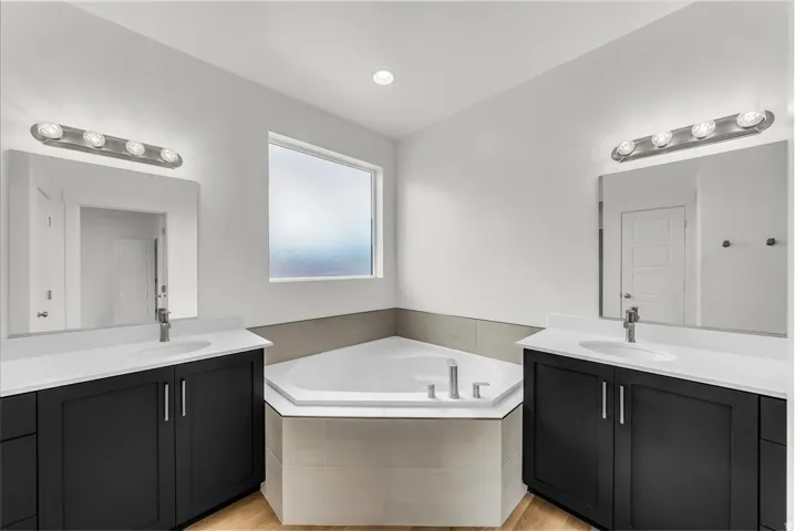 Dual vanities with undermount sinks, a corner soaking tub, and wood-finish flooring