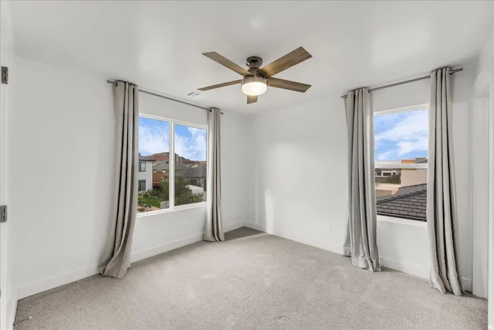 Plush carpeting, contemporary ceiling fan, and bright windows