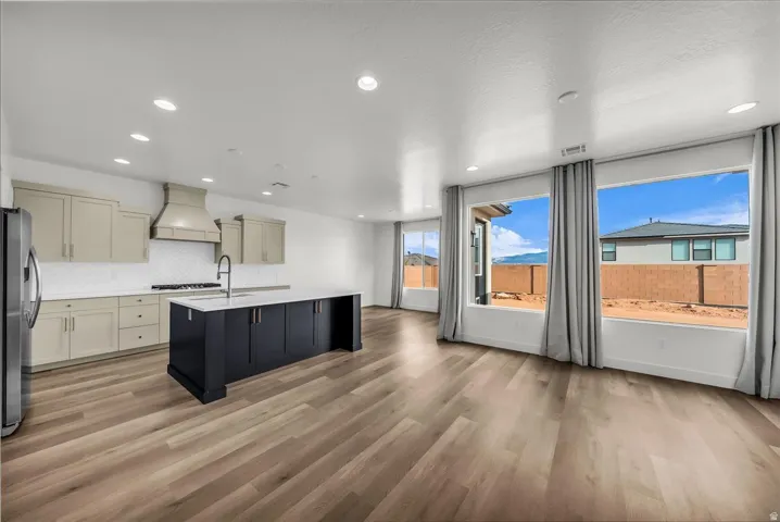 Open-concept living space with wood-finish flooring, recessed lighting, and a kitchen featuring a dark-toned island with a white countertop