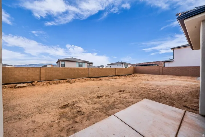 Expansive backyard with a concrete patio, block perimeter fencing, and distant mountain scenery