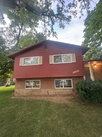 Charming split-level home featuring a brick foundation, burgundy exterior siding, and multiple windows providing natural light throughout