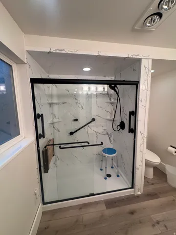 Shower with marble-patterned walls, matte black fixtures, and a clear glass enclosure