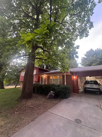 Split-level exterior with brick and siding facade, covered carport, concrete driveway, and mature landscaping