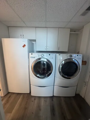 White wall-mounted cabinetry, white front-loading washer and dryer, and wood-finish flooring