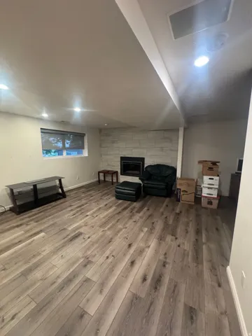 Wood-finish flooring, recessed lighting, and a fireplace with a stone surround