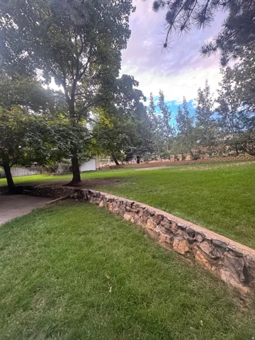 Expansive lawn area with a natural stone retaining wall and mature trees