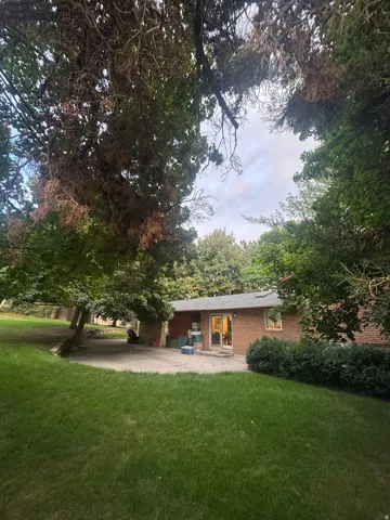 Backyard featuring a green lawn, mature trees, a concrete patio, and a brick exterior with a sliding glass door
