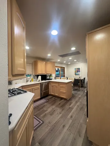 Kitchen featuring wood-finish flooring, light wood cabinetry, white countertops, a gas range, and stainless steel appliances