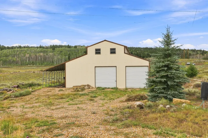 Metal barn structure featuring two roll-up garage doors, a covered side extension, and upper-level windows