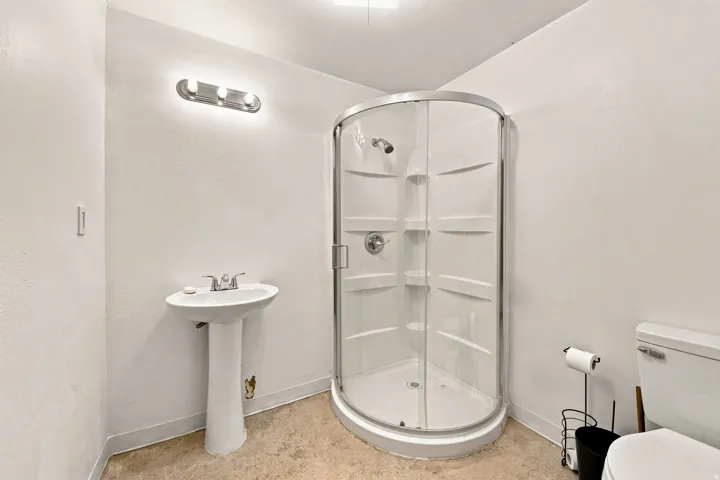 Pedestal sink, curved glass shower enclosure, white toilet, and recessed ceiling light