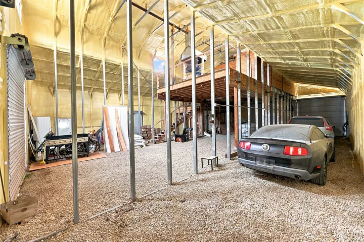 Large insulated garage structure with gravel flooring, exposed metal framing, and a partial upper-level loft