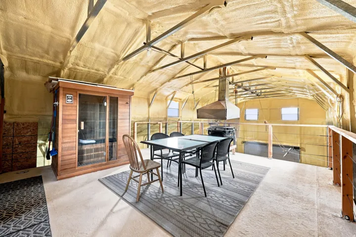 Vaulted ceiling with exposed structural beams, dedicated sauna unit, interior balcony with cable railing, integrated ventilation hood, and concrete flooring