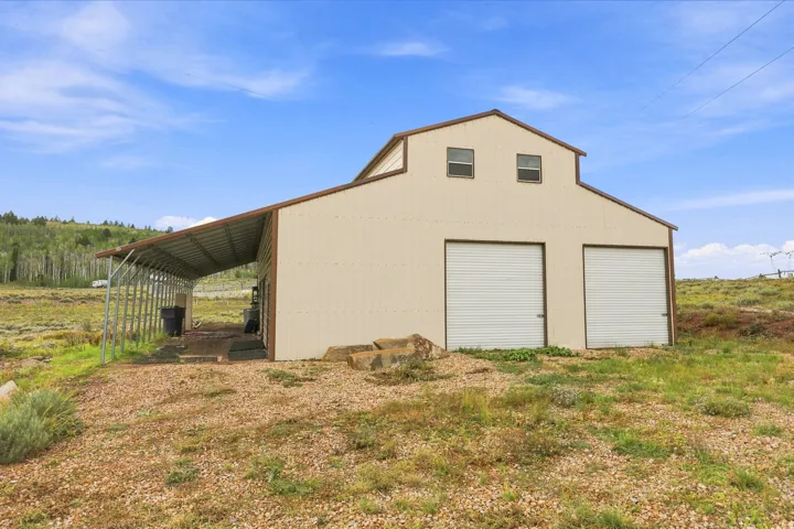 Two-story barn structure featuring a light-colored exterior, two roll-up garage doors, a covered side extension, and upper-level windows