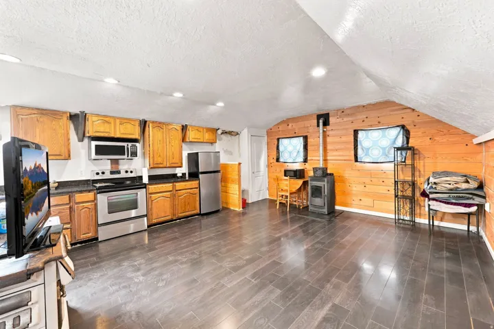 Wood-finish flooring throughout, stainless steel appliances, wood-paneled accent wall, recessed lighting, and a wood-burning stove