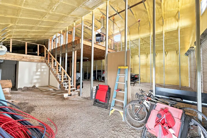 Open-concept space featuring a wood-frame staircase and second-level platform, exposed metal structural beams, and spray foam insulation on walls and ceiling