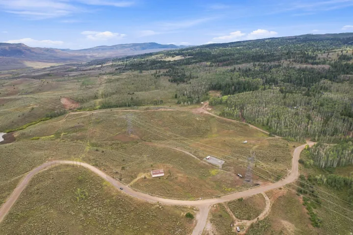 Expansive acreage featuring natural terrain, mature tree lines, a visible dirt road network, and distant mountainous topography