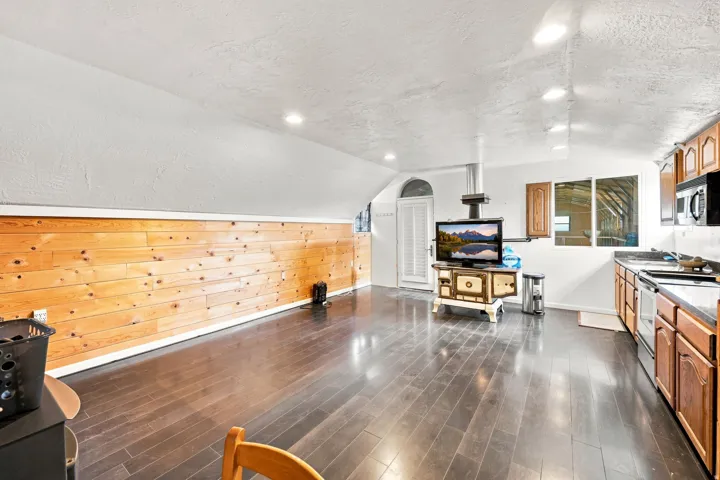 Dark wood-finish flooring with accent wood-paneled wall, recessed lighting, and built-in kitchen cabinetry with stainless steel appliances
