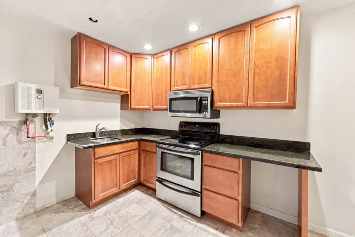 Built-in stainless steel microwave, stainless steel electric range, wood-finish cabinetry, dark stone countertops, and tile flooring