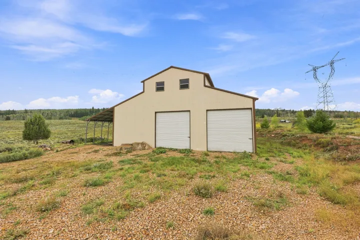 Metal barn structure featuring a gabled roof, two roll-up garage doors, and an attached side shed