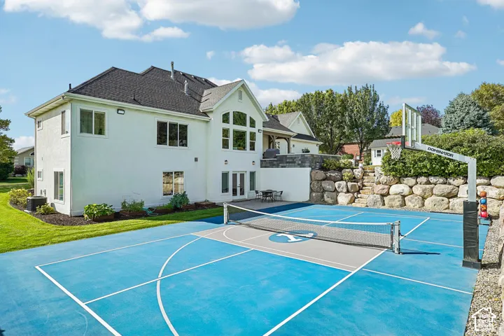 Expansive exterior featuring a multi-sport court with a basketball hoop and net, a stone retaining wall, and a raised patio area