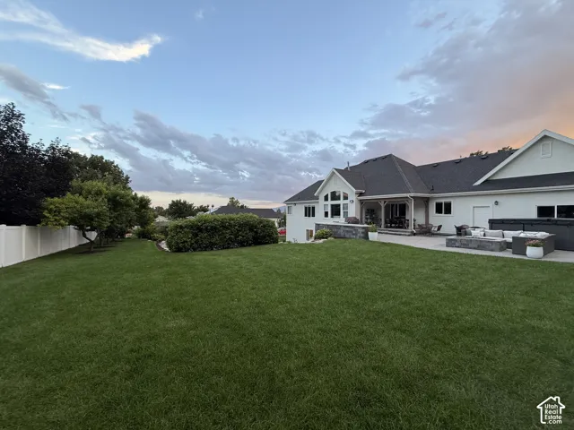 Expansive green lawn, white perimeter fencing, mature trees, multi-level patio with dark stone retaining walls, and a built-in outdoor spa