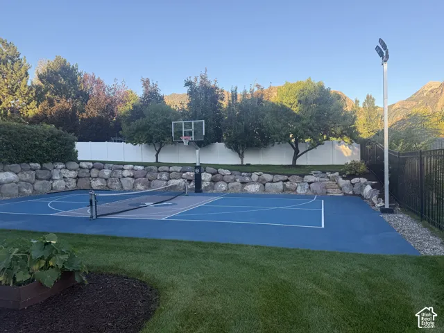 Multi-sport court with basketball hoop and net, complemented by a rock retaining wall and manicured lawn