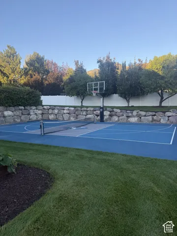 Multi-sport court with basketball hoop and net, surrounded by a stone retaining wall and mature trees